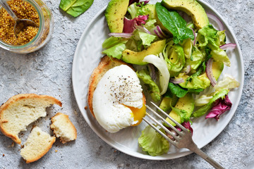 Fresh salad with spinach, avocado, egg plow and sauce on a concrete background. View from above.