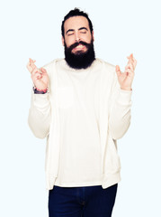 Fototapeta premium Young man with long hair and beard wearing sporty sweatshirt smiling crossing fingers with hope and eyes closed. Luck and superstitious concept.