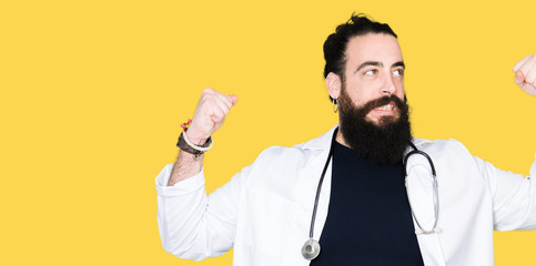 Doctor with long hair wearing medical coat and stethoscope showing arms muscles smiling proud. Fitness concept.