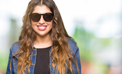 Young beautiful woman wearing sunglasses with a happy and cool smile on face. Lucky person.