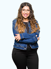 Obraz premium Young beautiful woman wearing glasses and denim jacket happy face smiling with crossed arms looking at the camera. Positive person.