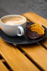 cup of coffee on wooden table and orange with chocolate on a black plate
