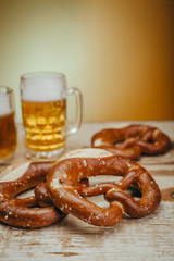 draft beer in the mugs and pretzels on wooden board against yellow background