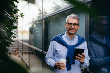 middle aged businessman using tablet and drinking coffee to go outdoor