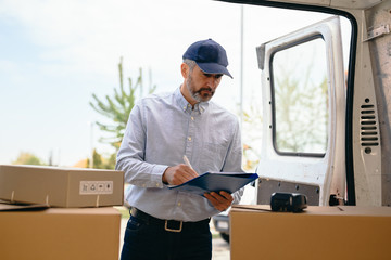 middle aged courier looking at the trunk of his vehicle for a packages