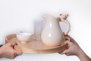 Hand holding tray with jug and ceramic bowl isolated on white background