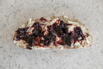 Top view of simple breakfast, a slice of homemade bread with butter and plum jam