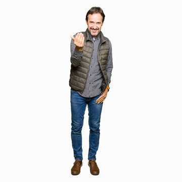 Middle age handsome man wearing winter vest Beckoning come here gesture with hand inviting happy and smiling