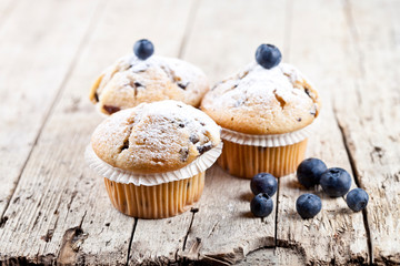 Homemade fresh muffins with blueberries on rustic wooden table.