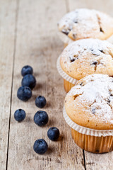 Homemade fresh muffins with blueberries on rustic wooden table background.