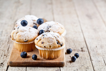 Four homemade fresh muffins with blueberries on rustic wooden table background.