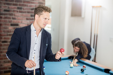 Modern man with pool ball standing next to snooker table.