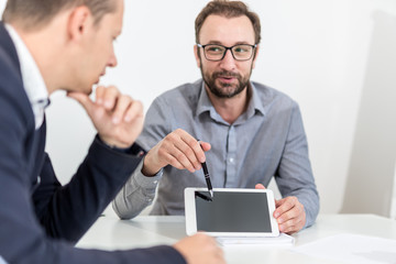 Fototapeta premium Two businessman using blank screen tablet device while sitting at the desk on a meeting.