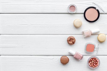decorative cosmetics for make-up with macaroon cookies on white wooden tabletop background mock up