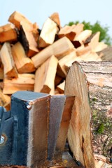 close up of wedge and knife of wood splitter about to cut through a block of hard maple with heap of split wood in behind