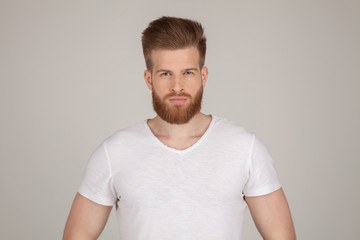 Obraz premium Serious thoughtful male with ginger beard, dressed casually, looking to the camera, isolated over white brick wall background