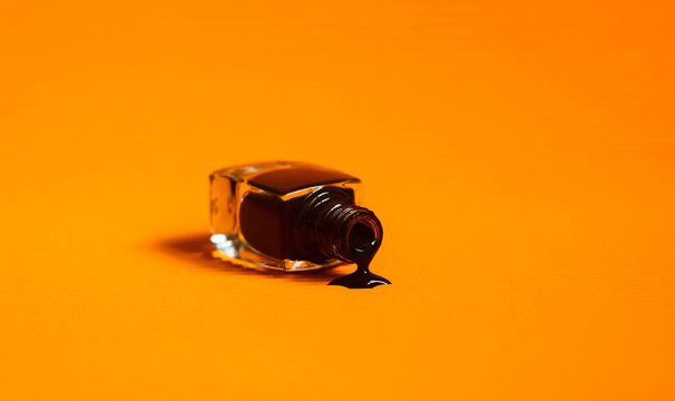 Dark Nail Polish Spilled From The Bottle. Vibrant Orange Background.