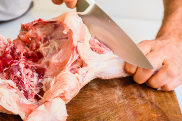 Butcher chopping a raw chicken with a large knife.