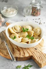 Meat dumplings - russian pelmeni, ravioli with meat on a white plate on a wooden board