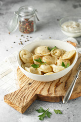 Meat dumplings - russian pelmeni, ravioli with meat on a white plate on a wooden board