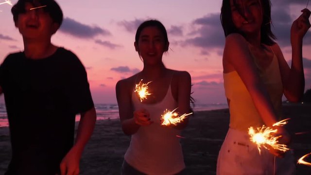Asian teen group dancing and playing firework seaside together in beach summer with sunset background. Young asia happy emotion and anniversary celebration. 4K resolution and slow motion.
