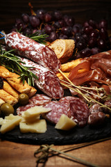antipasto various appetizer. Cutting board with prosciutto, salami, cheese, bread and olives on dark wooden background