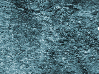 blue pebbles and ripples on running water with light reflected on the surface