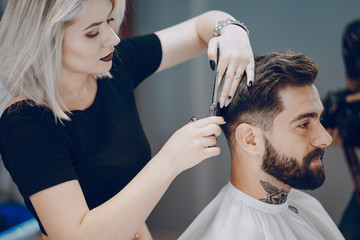 handsome young bearded guy sitting in an armchair in a beauty salon and the girl near him cuts his...