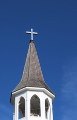 Fototapeta na wymiar Bell tower and church steeple with stainless steel cross on top isolated on blue sky