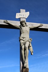 Outside life size crucifix of Jesus on wooden weathered cross on sunny day with blue sky
