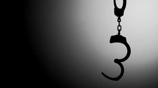 OPEN HANDCUFFS HANGING IN SILHOUETTE, WITH NEGATIVE SPACE.  IN 4K.