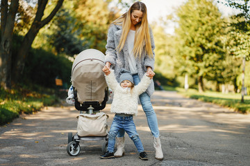 young blonde mother walking and playing with her toddler daughter and pushing a stroller through...