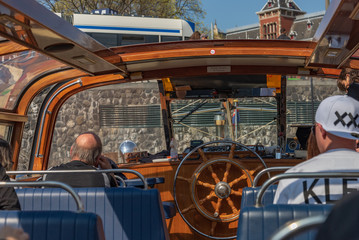 Interior view canal cruise tour float at pier with wooden decorated wall and steering wheel, and opening glass windows and sky lights, and tourist sit on seat in Amsterdam, Netherlands.