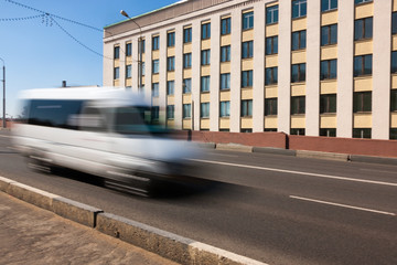 Motion of a blurred white minibus on the highway during the daytime