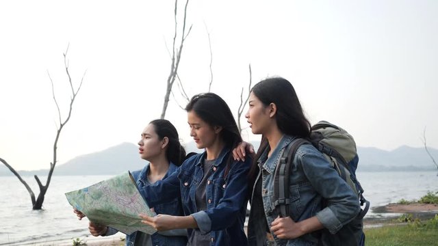 Three asian young women holding a paper map for navigation in summer lake together. Travelers monitoring travel route. Concept of travel holiday, navigate and geographic.