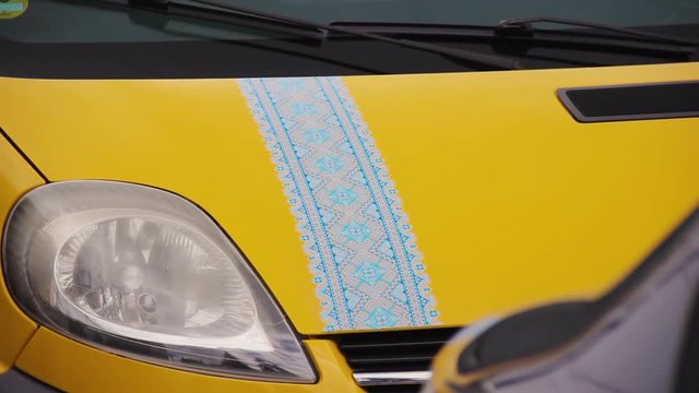 Yellow minivan with applique on the hood in the form of a national Ukrainian pattern. Popular in the period of Maidan embroidery on the car body. Vinyl decal decoration with traditional ornament print