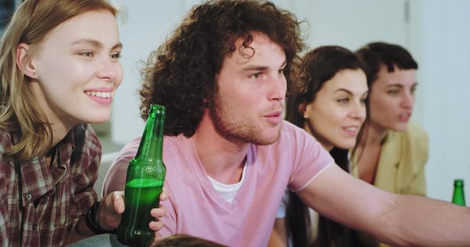 Portrait of charismatic young group of friends in front of TV support their best football team very emotional they are excited how the team play yelling and cheers with beer bottles in a very friendly