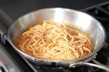 Spaghetti pasta with meat sauce, cooking in a stainless steel pan, on the stove.
