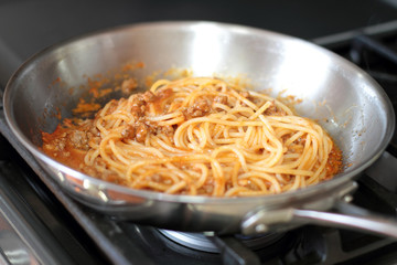 Spaghetti pasta with meat sauce, cooking in a stainless steel pan, on the stove.