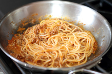 Spaghetti pasta with meat sauce, cooking in a stainless steel pan, on the stove.