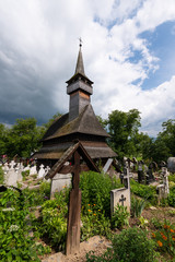 Fototapeta na wymiar Ieud, Maramures, Romania - July 9, 2018: Ieud Hill Church and its graveyard, the oldest wood church in Maramures, Romania under a dramatic sky.