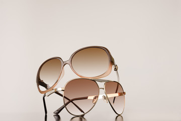 Two pairs of womens sunglasses stacked on top of each other with plain background