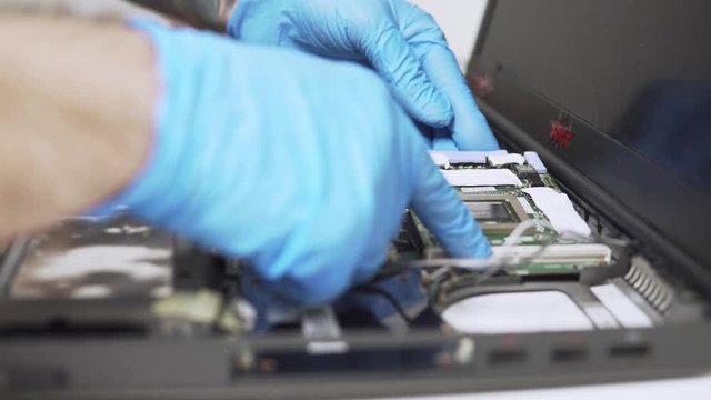 A static view of Technician IT worker is fixing an old laptop with protective gloves and installing new parts.