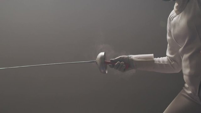 Male and female fencers train in a dark and dusty fencing gym