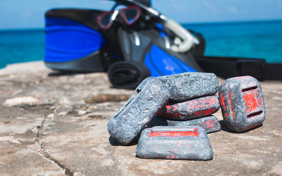 Scuba diving weights on rock by the ocean with equipment in background