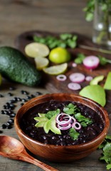black bean soup or stew. Latin American or Mexican cuisine. stewed black beans served with avocado and red onion and cilantro.