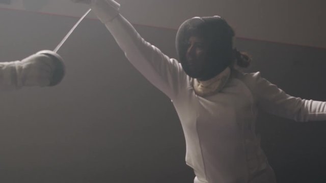 A female fencer attacks and parrying in a dark and dusty fencing gym