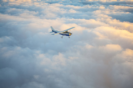 Small single engine airplane flying in the gorgeous sunset sky through the sea of clouds