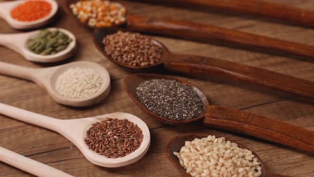 Various seeds and grains in wooden spoons on the table - camera slide, diversified diet concept, close up