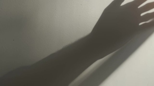 Man's hand moves over a wall with long shadow from window